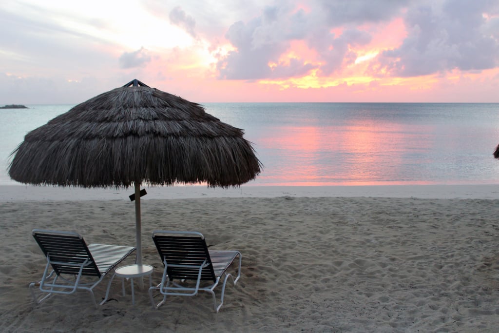 Two loungers under a thatched umbrella on a Cat Island beach at pink sunset
