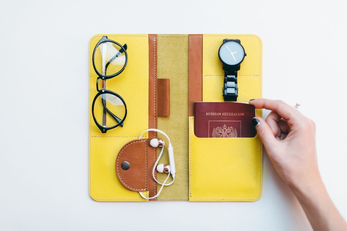 A yellow travel wallet organizer holding a passport, glasses, watch, and earbuds.