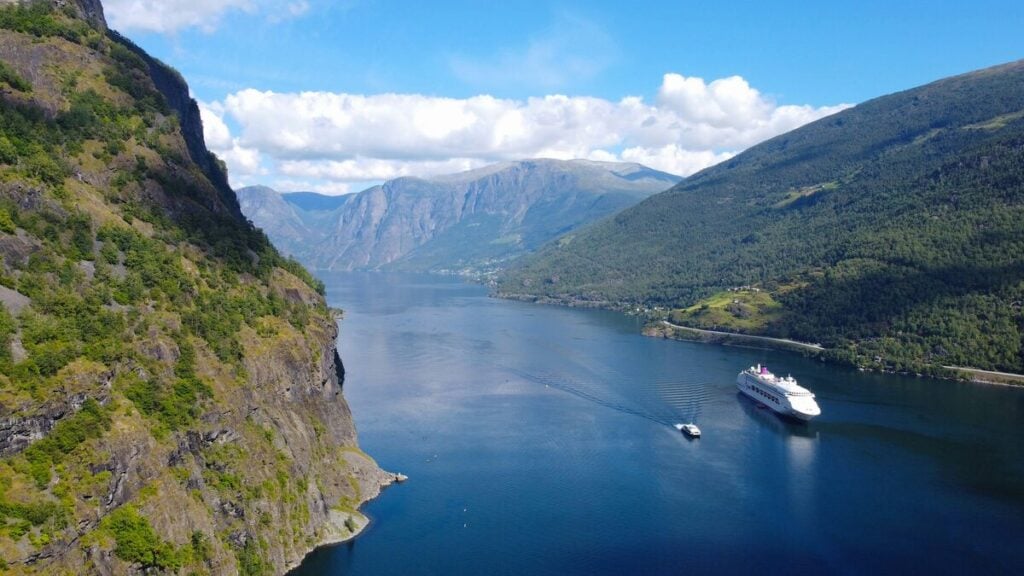 Aerial view of a cruise ship and a smaller tour boat on the Aurlandsfjord surrounded by steep green mountains.
