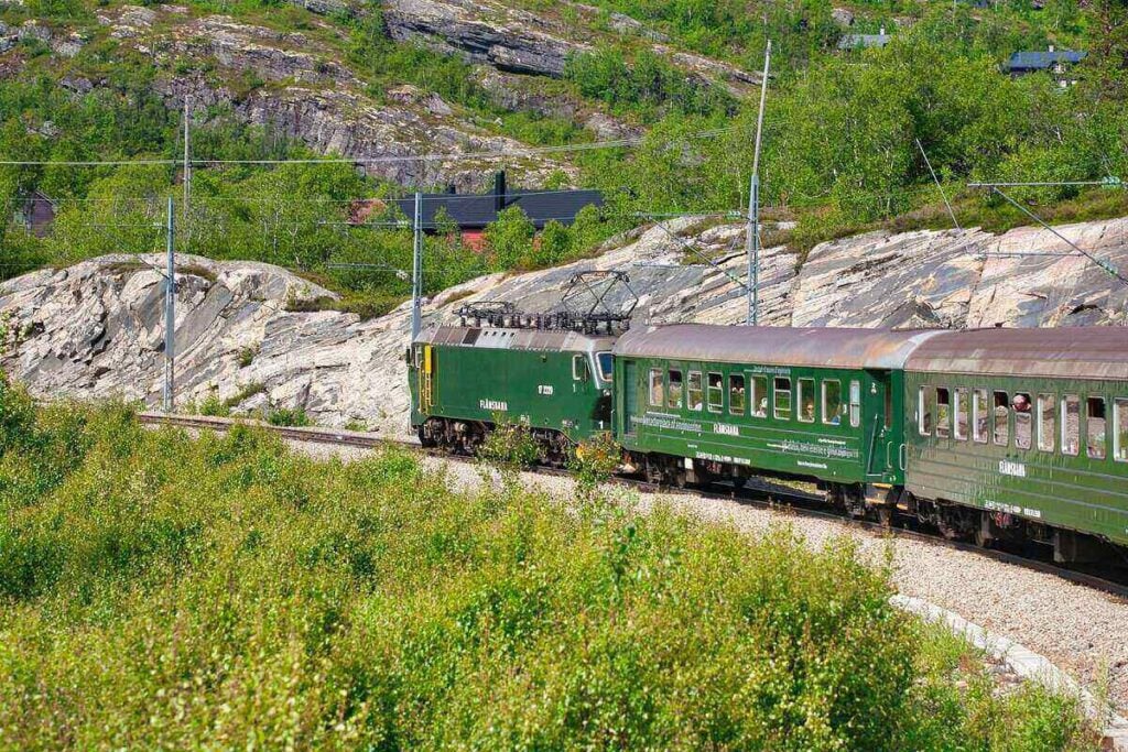 Green Flamsbana train on the tracks surrounded by rocky mountain terrain