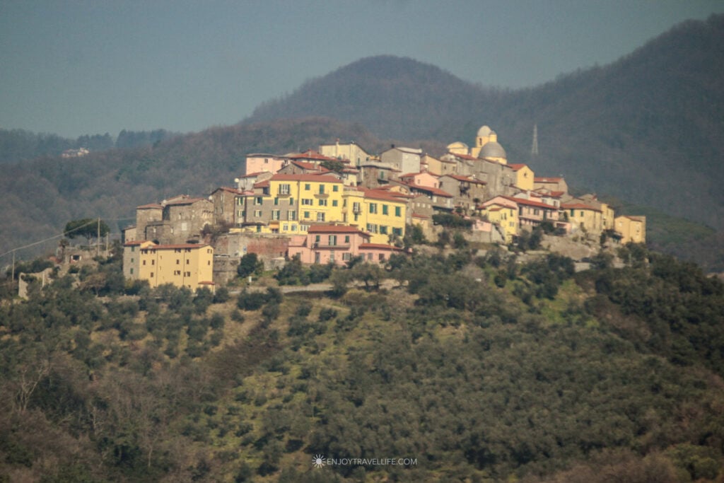 Hilltop village of Borgo di Nicola with domed church and colorful buildings on olive-covered slopes seen from the train to Cinque Terre