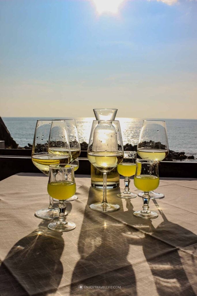 Glasses of limoncello and white wine on a waterfront restaurant table with the Tyrrhenian Sea and late afternoon sun in Cinque Terre.