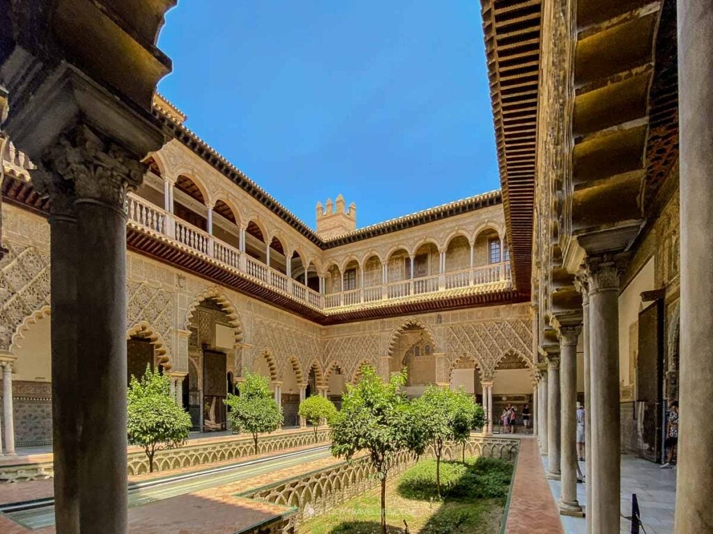 The Patio de las Doncellas in the Real Alcázar of Seville, with Moorish arches reflected in a long central pool.