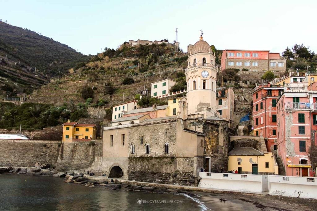 Church of Santa Margherita d'Antiochia and its octagonal bell tower at the waterfront in Vernazza Cinque Terre with terraced hillside above.