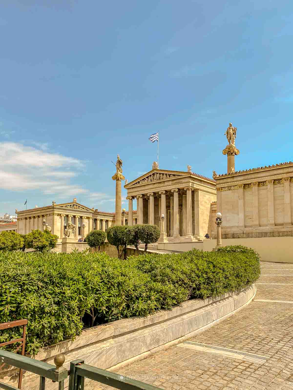 The neoclassical Academy of Athens stands with its marble columns and statues under a blue sky in Athens, Greece.