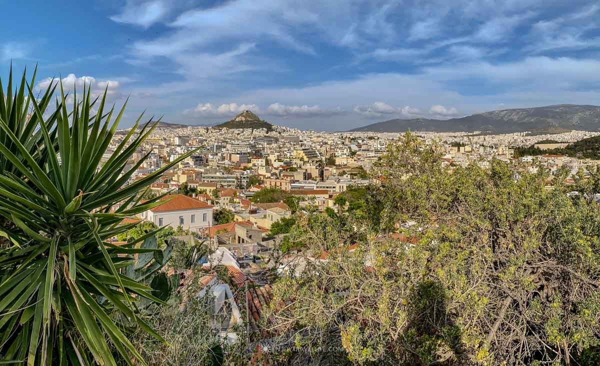 A view across the rooftops of Athens reaches Lycabettus Hill under a bright sky in Greece.