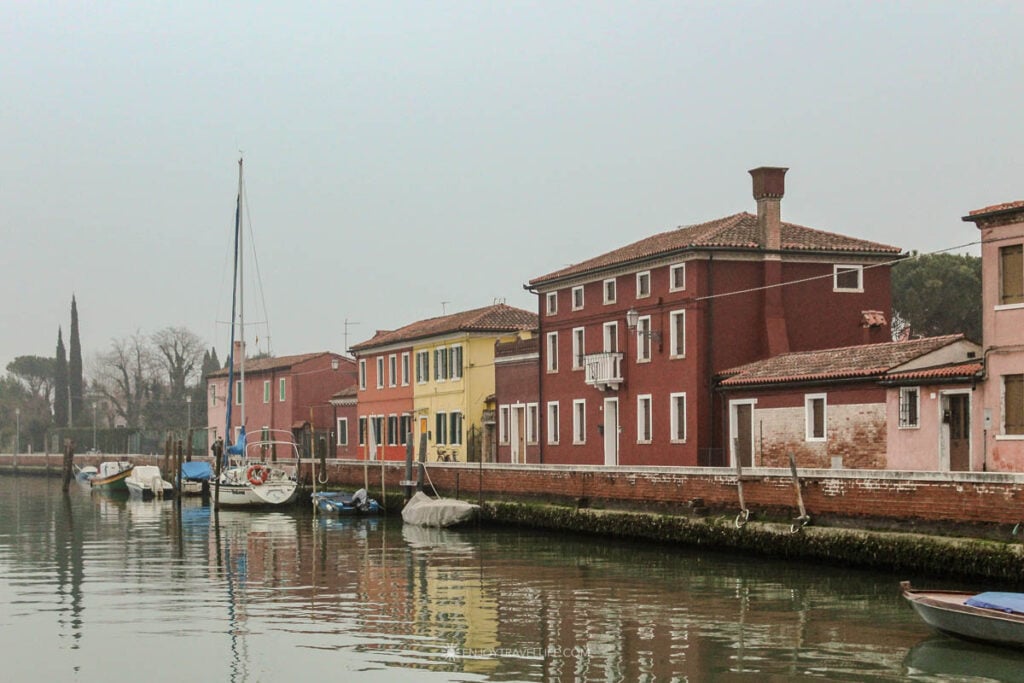 Colorful houses and moored boats line a Burano canal on a gray winter afternoon.