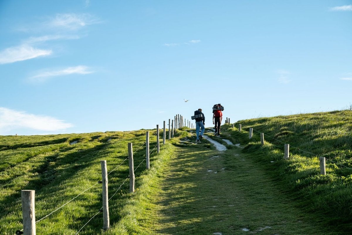 Two pilgrims with backpacks walk a stone path together on the Camino de Santiago.
