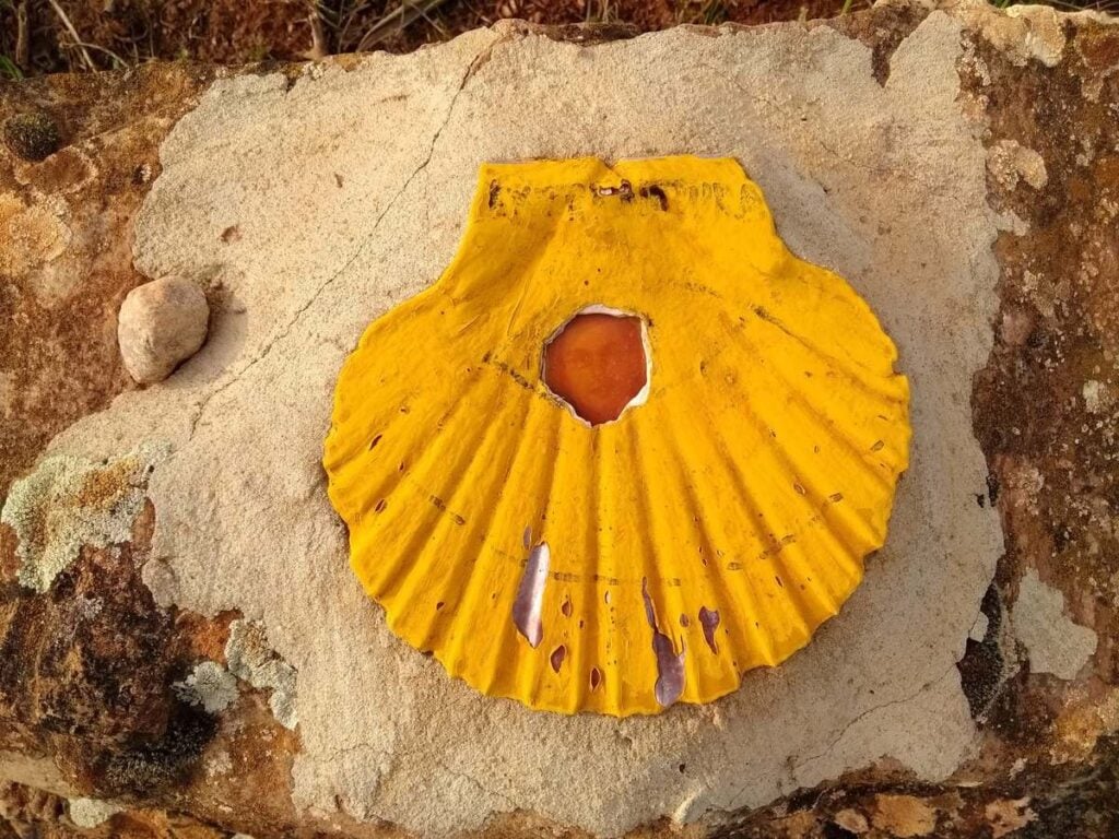 A yellow scallop shell painted on stone marks the route of the Camino de Santiago.