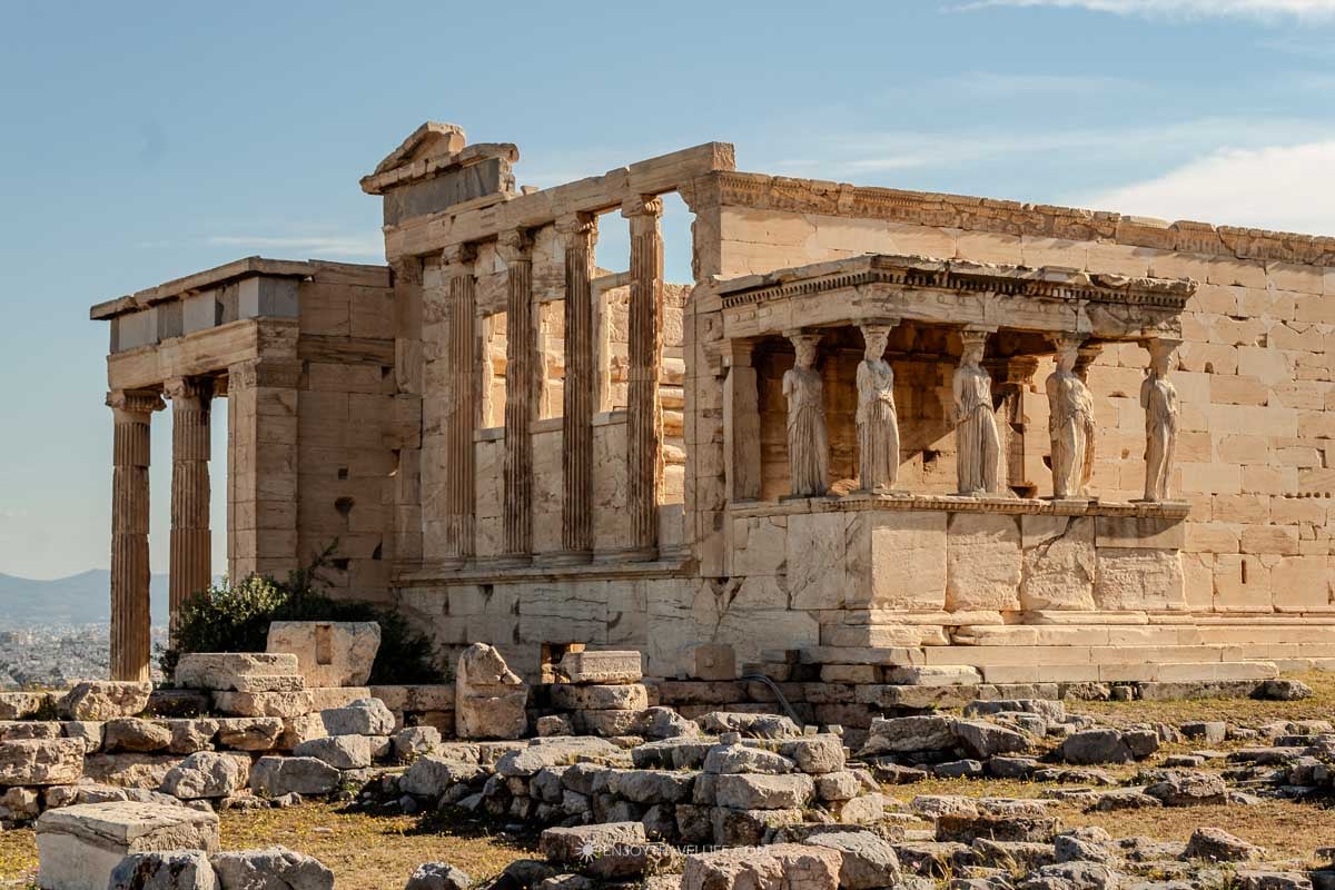 The Erechtheion temple and its Caryatid porch stand on the Acropolis under a blue sky in Athens, Greece. (Athens City Guide)