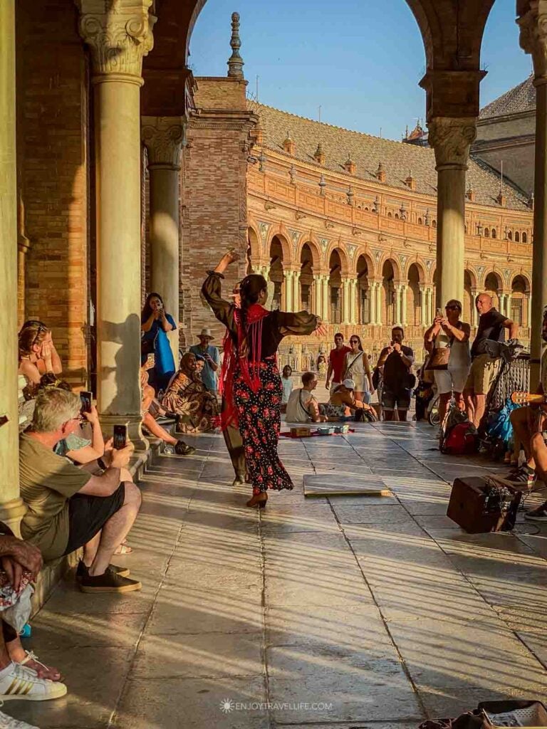 A flamenco dancer in a red shawl performs for a small crowd in the Plaza de España in Seville, Spain.