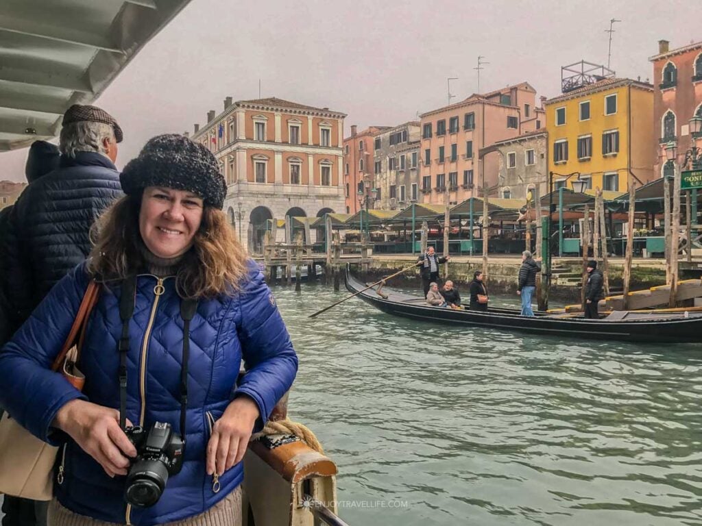 Jackie Gately stands bundled in a winter coat along the Grand Canal in Venice, with gondolas and palazzos behind her.