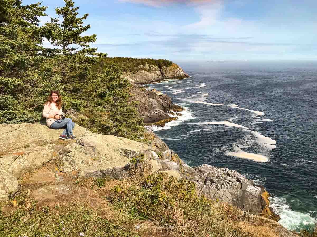 A traveler sits on the granite ledges of Monhegan Island's far shore with the spruce headland and crashing surf behind.