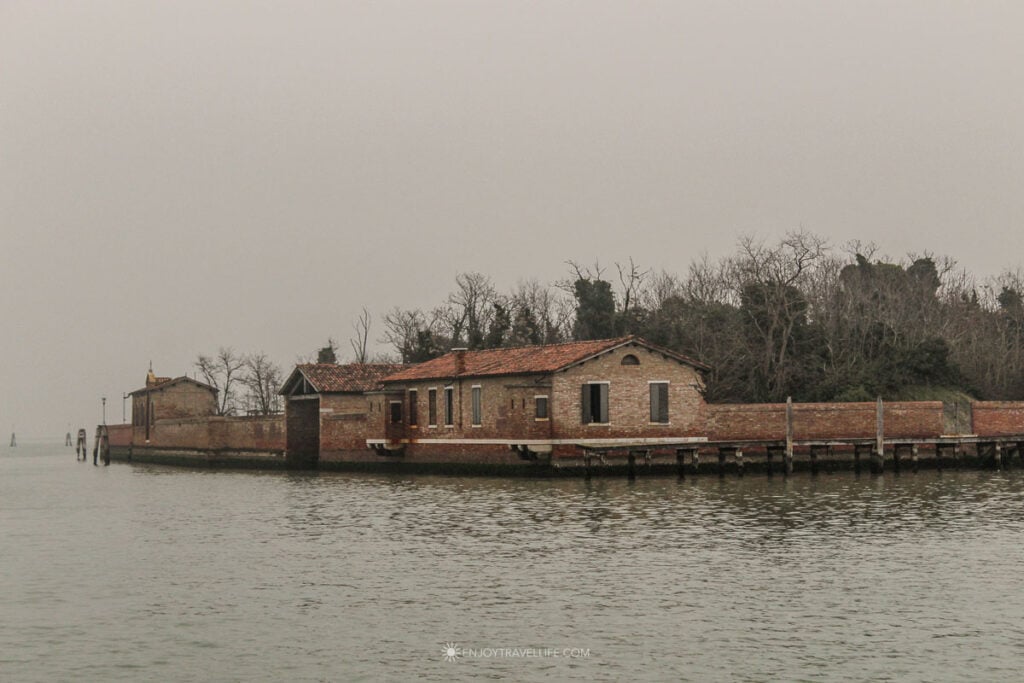 A lone brick building stands on a small island in the Venice lagoon, seen from the vaporetto on a foggy winter day.