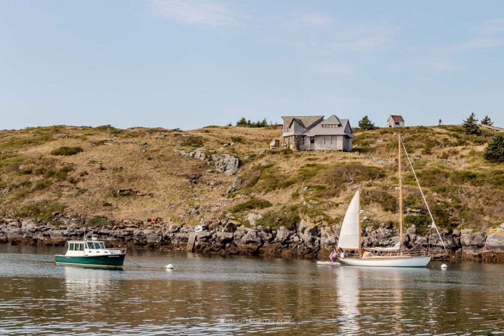 Manana Island rises green and rocky across the channel on the approach to Monhegan Island, with boats at their moorings.