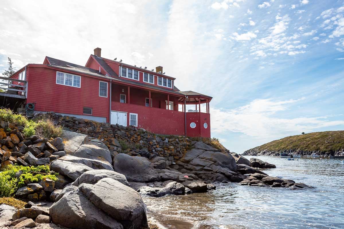 A large red house stands on the rocky shore at the water's edge on Monhegan Island.