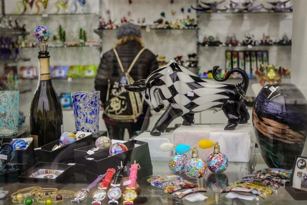 A table displays small, affordable Murano glass pieces, including pendants and animal figurines in many colors.