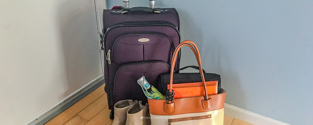 A packed suitcase with ankle boots and a tan-and-cream tote bag ready by the door