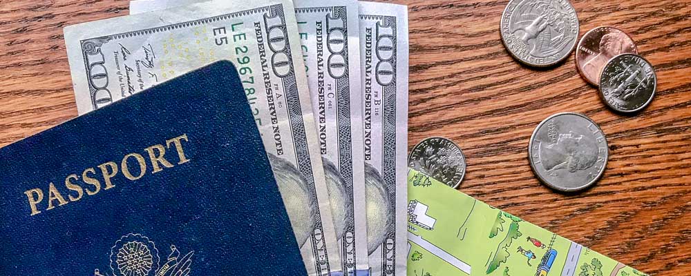 A US passport, three hundred-dollar bills, coins, and a travel map on a wooden table