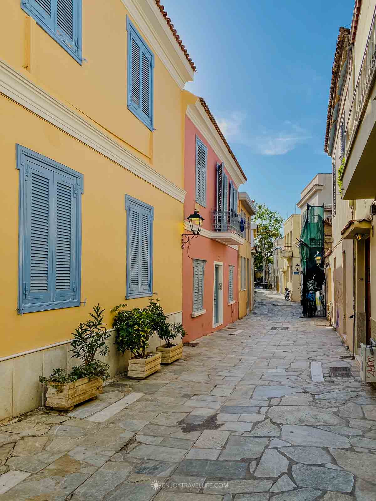 A narrow Plaka lane is lined with pastel neoclassical houses and blue shutters in central Athens, Greece.