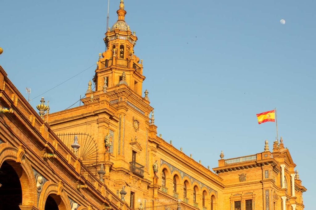 A tower of the Plaza de España flies the Spanish flag at golden hour in Seville, Spain.