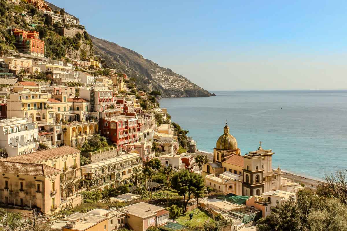 Colorful buildings of Positano cascading down the hillside to the turquoise Amalfi Coast with a golden-domed church in the foreground