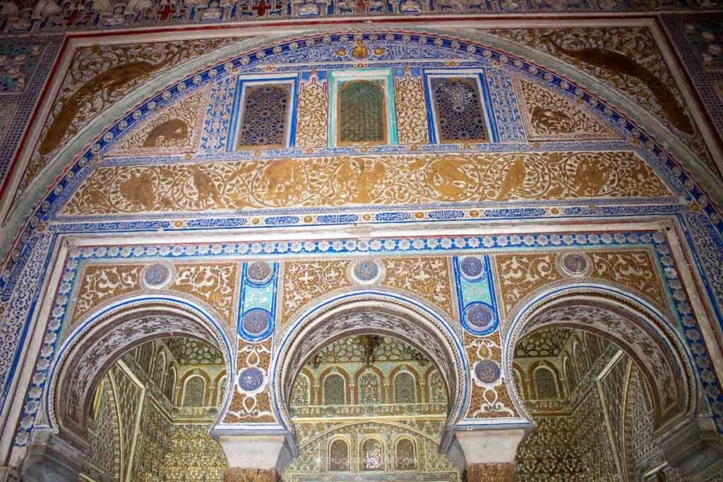 Carved Moorish arches and blue-and-gold tilework inside the Real Alcázar of Seville, Spain.