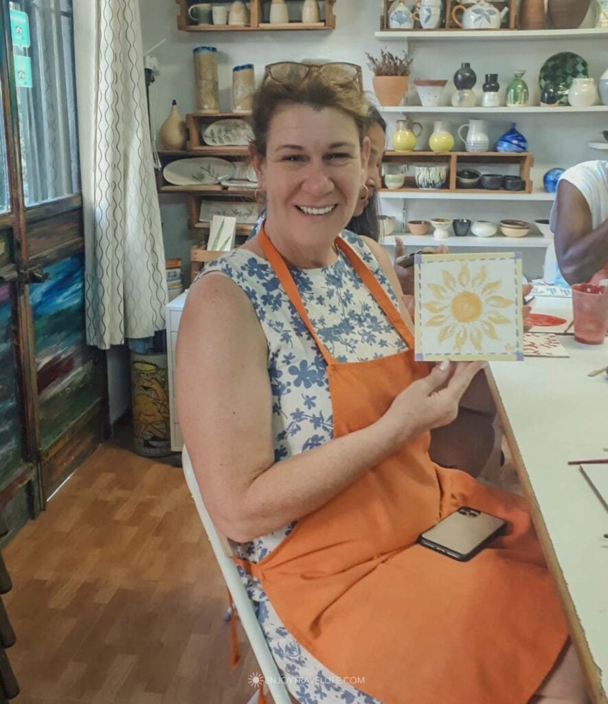 A visitor holding a hand-painted sun azulejo tile at a ceramics workshop in Triana, Seville.