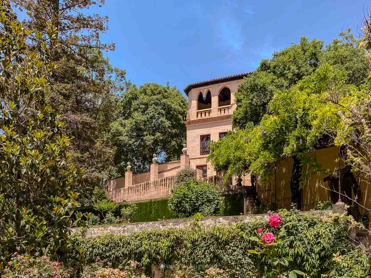Stone tower with arched windows surrounded by lush gardens and pink roses in Spain