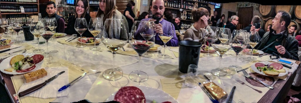 Guests seated around a communal table during a wine tasting at Tenuta Torciano with glasses of red and white wine and Tuscan antipasti.