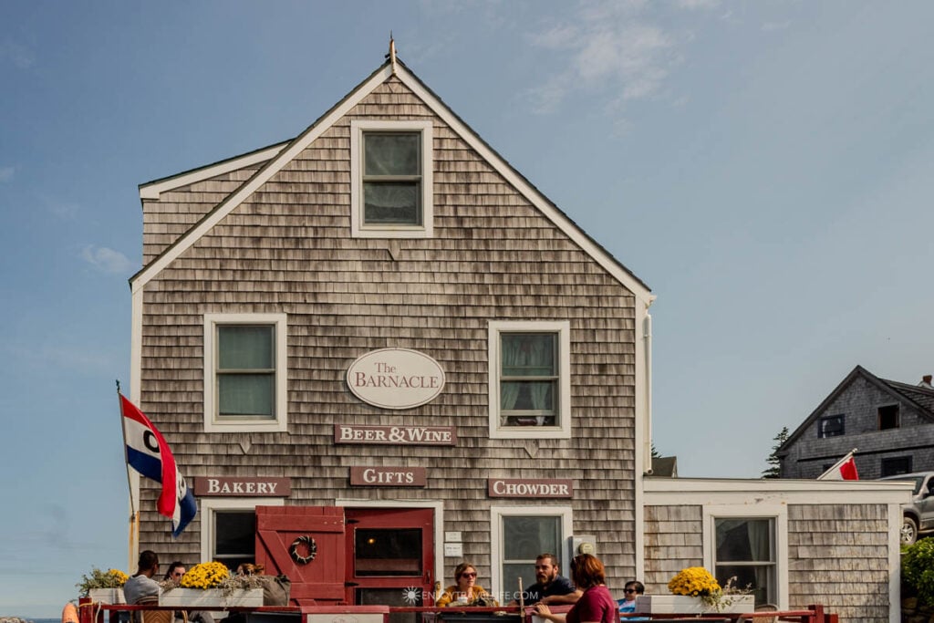 The Barnacle, a gray-shingled cafe by the wharf on Monhegan Island, with people seated at outdoor tables.
