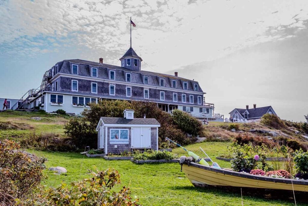 The Island Inn, a large gray-shingled hotel topped with a cupola, stands on a grassy rise on Monhegan Island, with a yellow dory and a small shed in the foreground.