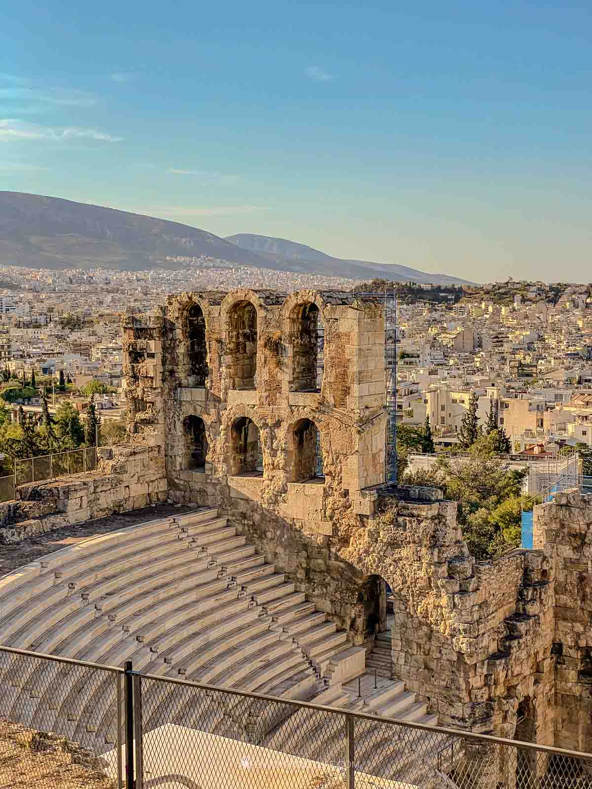The stone tiers of the Theater of Herodes Atticus curve below the Acropolis with the city of Athens beyond.