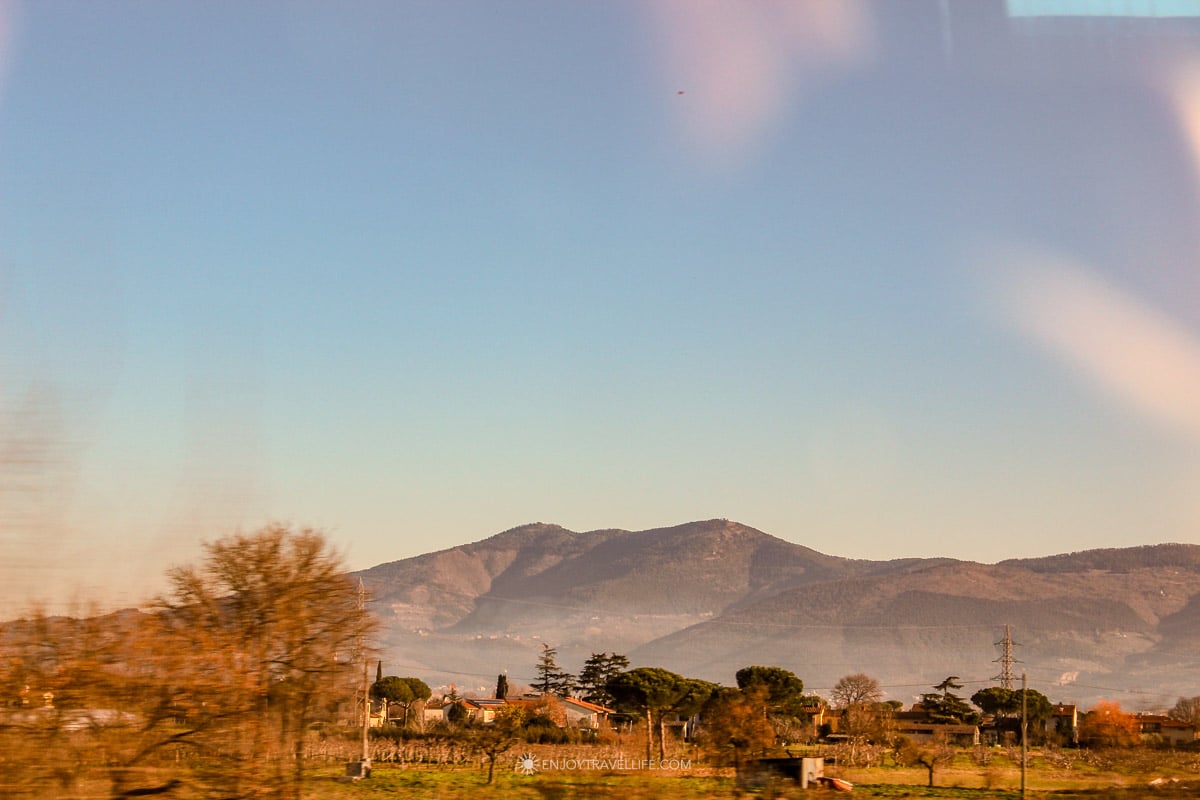 Tuscan countryside with rolling golden hills and cypress trees seen from the tour bus window