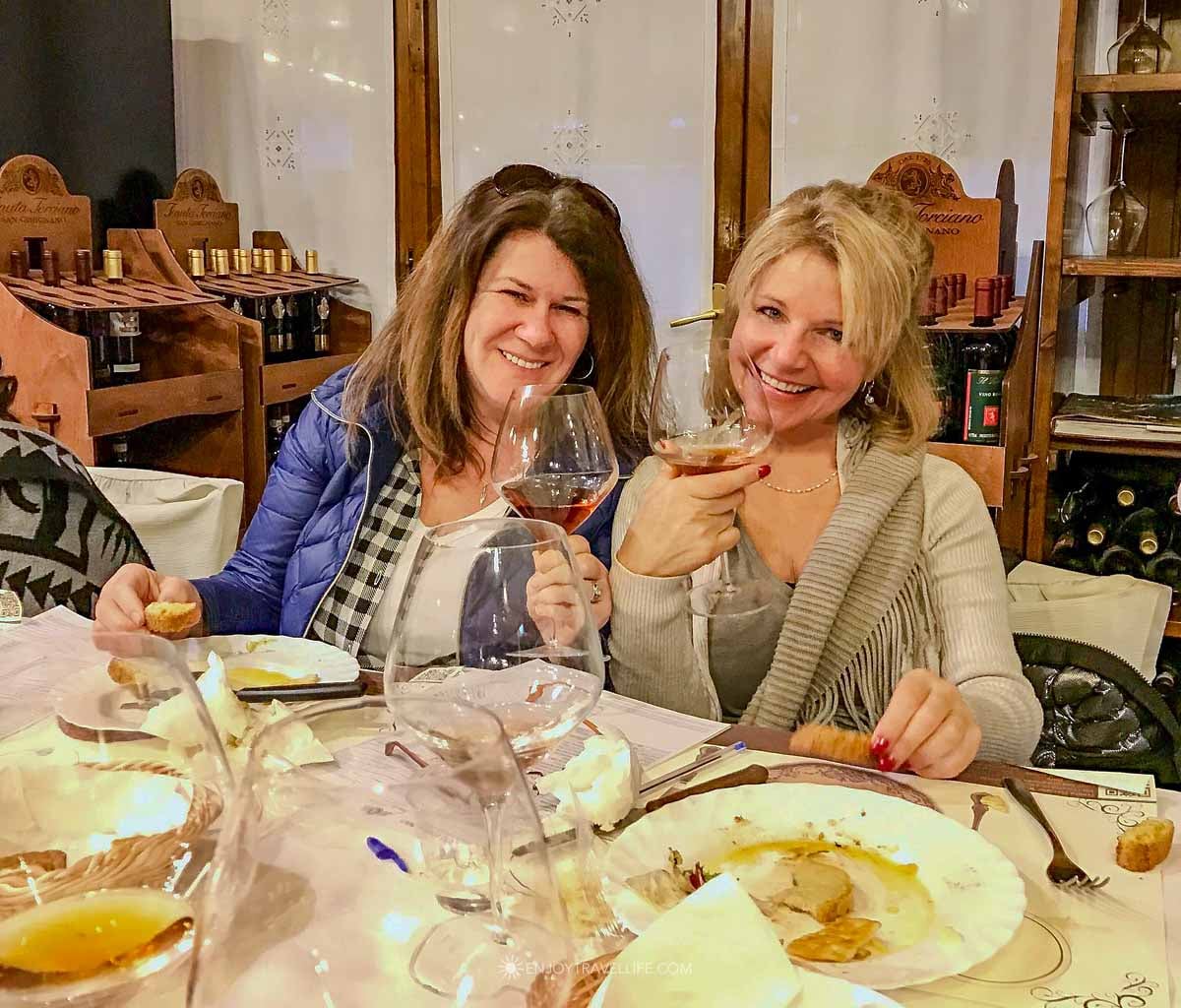 Two women smiling and raising wine glasses at the communal tasting table at Tenuta Torciano winery