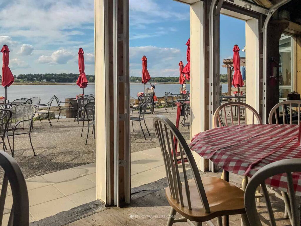 The open-air dining room at Cook's Lobster & Ale House on Bailey Island, Maine looks out past red umbrellas to Casco Bay.