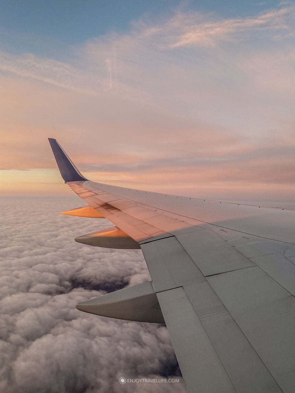 An airplane wing catches golden light above a blanket of pink sunset clouds.