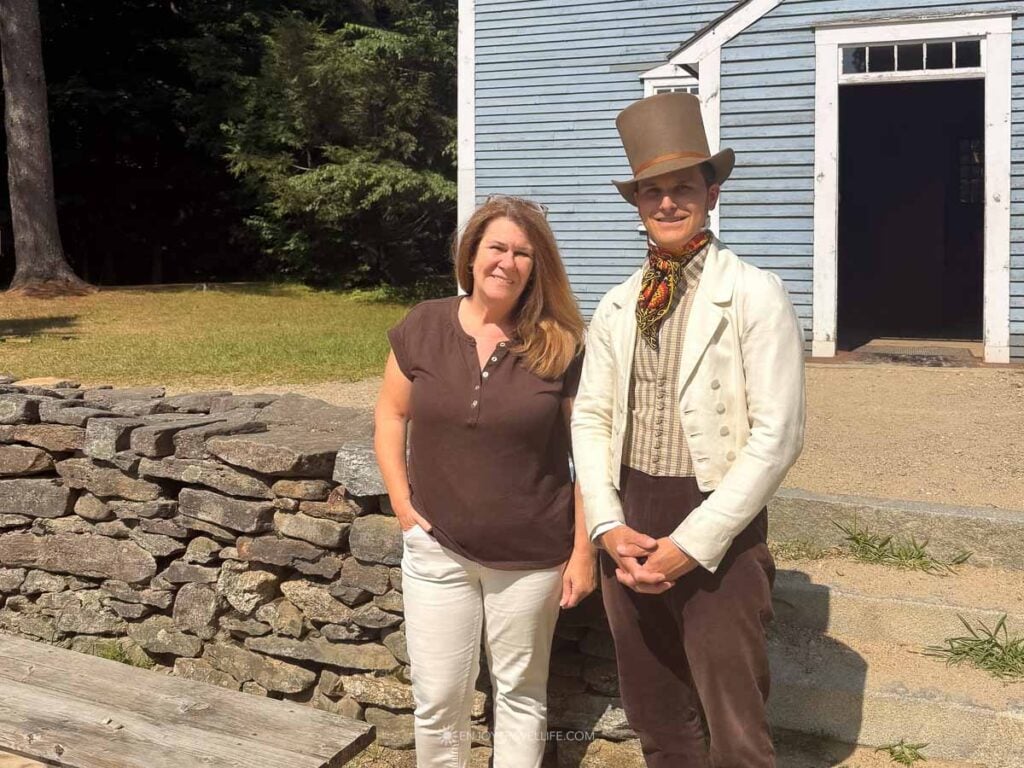 Jackie Gately visits with a costumed townsperson outside the blue schoolhouse at Old Sturbridge Village.