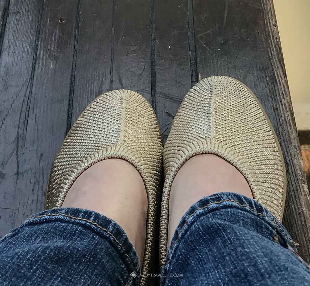 Knit ballet flats worn with cuffed jeans on a dark wood floor.
