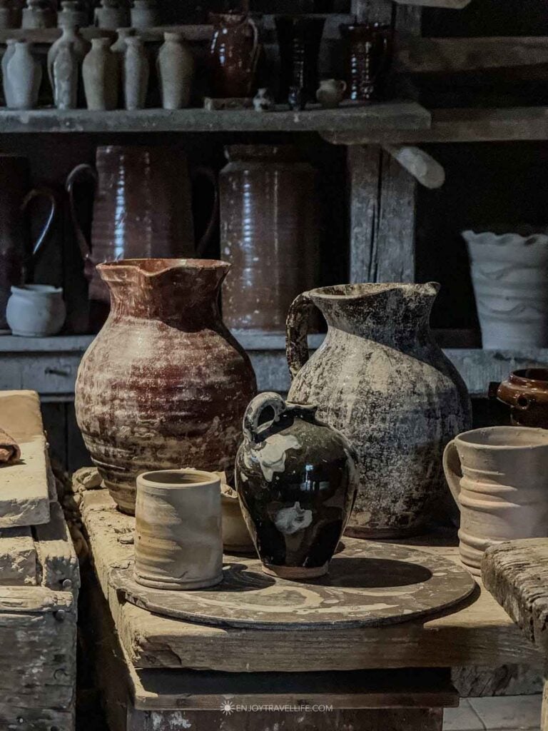 A fresh pot rests on the wheel beside finished redware in the pottery shop.