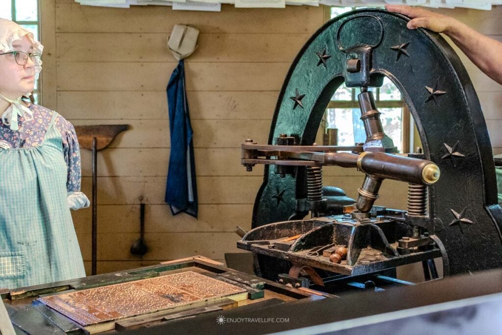 A costumed printer works the hand press in the printing office.