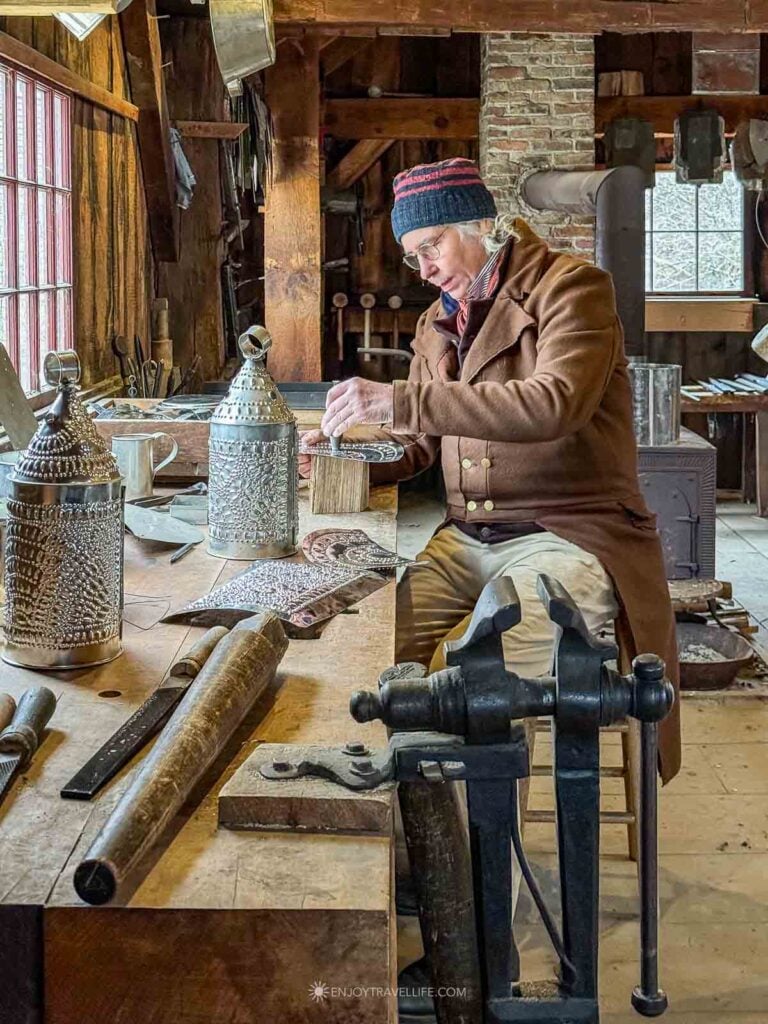 The tinsmith shapes pierced-tin lanterns at his workbench in winter.