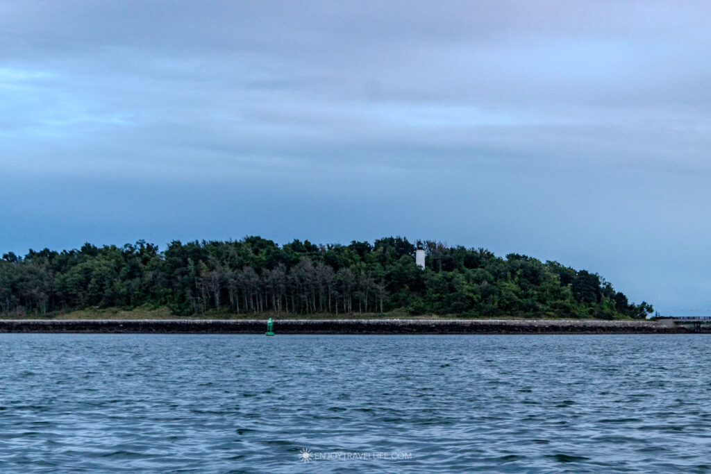 A wooded Boston Harbor island sits low and green on the horizon at dusk, seen from the water.