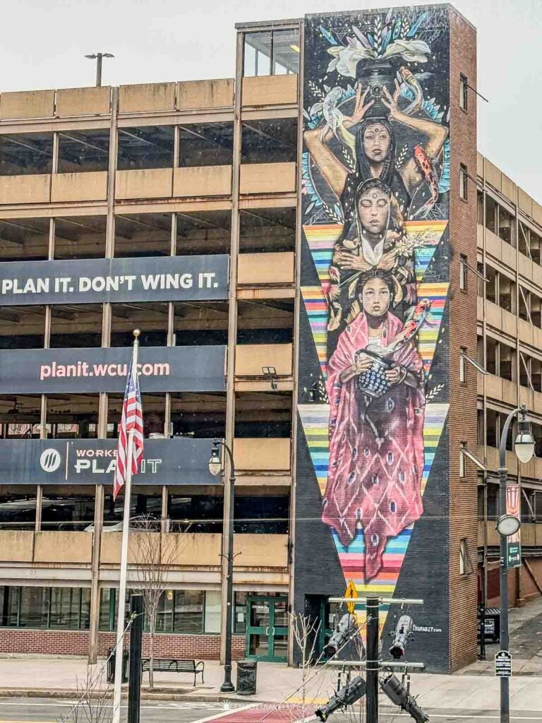 Colorful mural of three women rising several stories up a downtown Worcester parking garage.