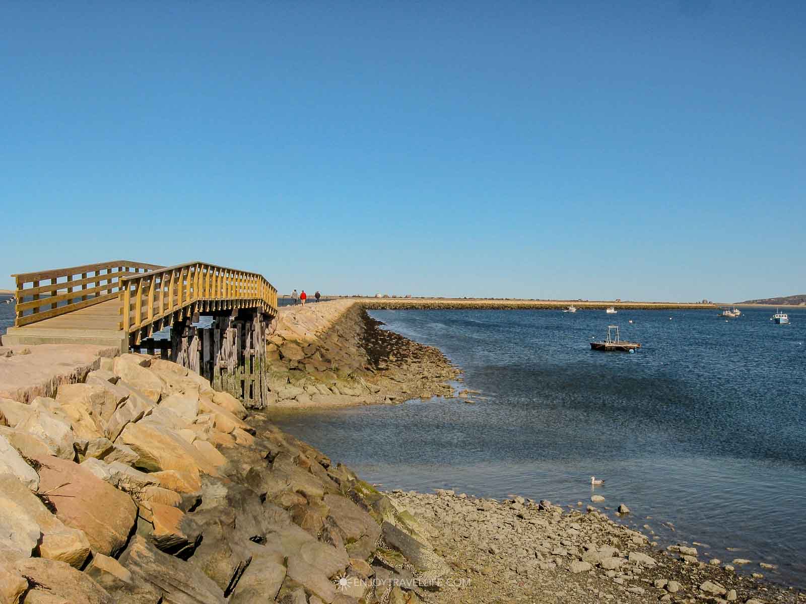A wooden footbridge leads walkers onto the stone jetty in Plymouth Harbor, one of the best things to do in Plymouth MA.