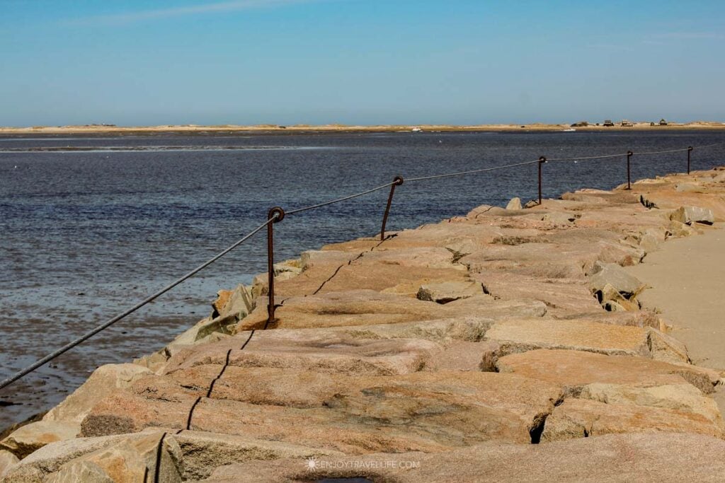 Iron rings and a steel cable line the granite breakwater in Plymouth Harbor, with the barrier beach in the distance.
