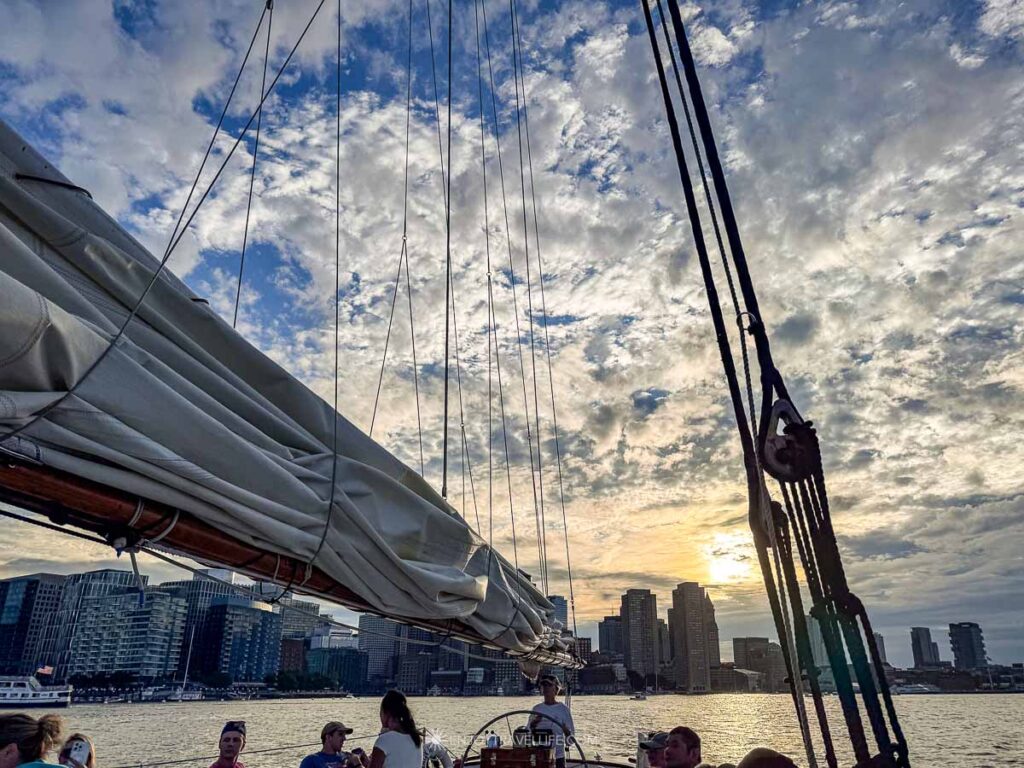 The schooner's boom and rigging cut across the Boston skyline under a wide mackerel sky.