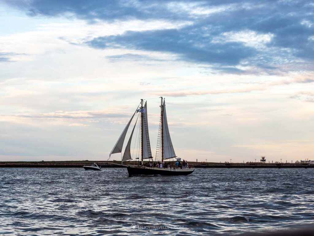 A two-masted schooner sails a parallel course across Boston Harbor in the evening light.