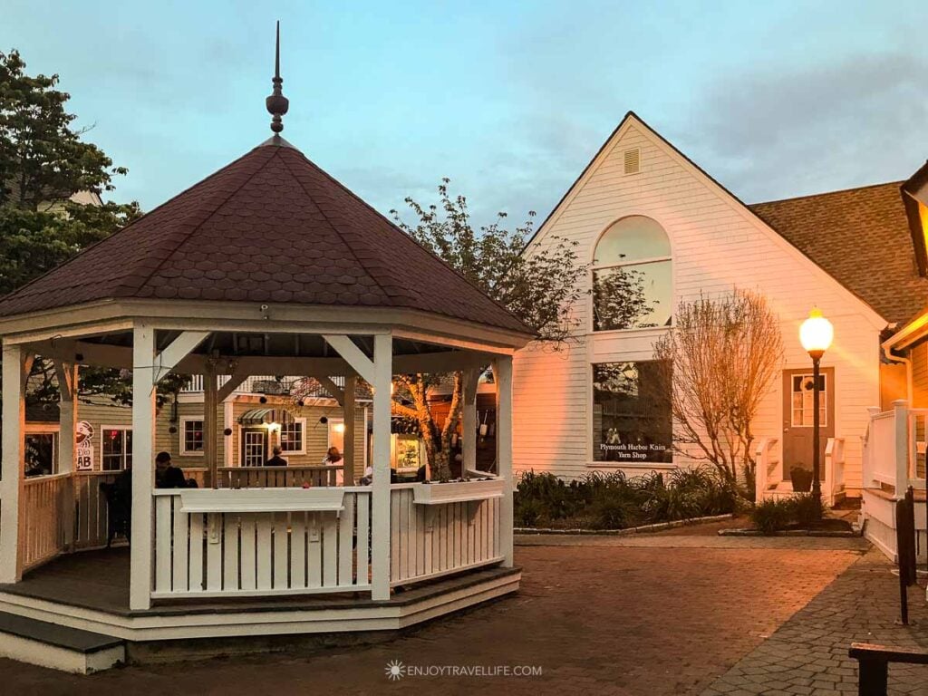 The gazebo at The Shoppes at Village Landing in Plymouth glows at dusk beside warmly lit storefronts.