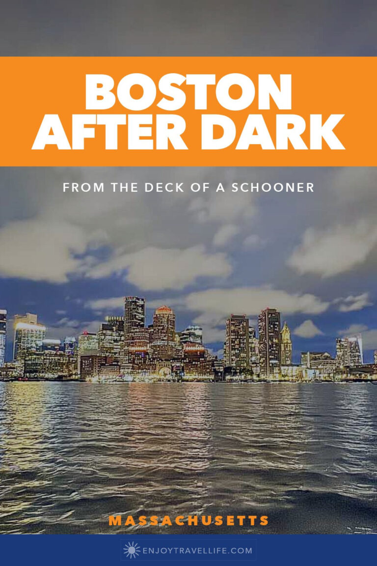 The Boston skyline lit up at night across the water from the deck of a schooner on Boston Harbor.